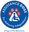 Assistance Dogs for Achieving Independence's logo. Along the inner edge of a blue circle is written "Assistance Dogs for Achieving Independence." In the middle of the circle is a paw print. In the large portion of the paw print is a silhouette of a person in a wheelchair. There are 4 paw print "toes" each with one letter in them making up the word "ADAI"