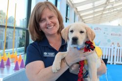 Stephanie is smiling at the camera. She is holding a small yellow labrador retriever puppy in her arms.