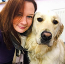 Hannah Plant is smiling at the camera. She is side-hugging a light yellow golden retriever. 