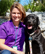 Victoria Cavaliere is smiling at the camera. She has her arm around a black labrador retriever. 