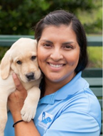 Zuhey is smiling at the camera. She is holding a yellow labrador retriever puppy in her arms so the puppy's face is next to hers. 