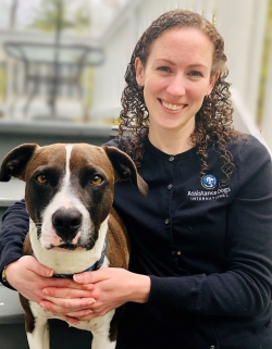 Laura Hilbert is smiling at the camera. She has her arms around a dog, who is also looking at the camera. 